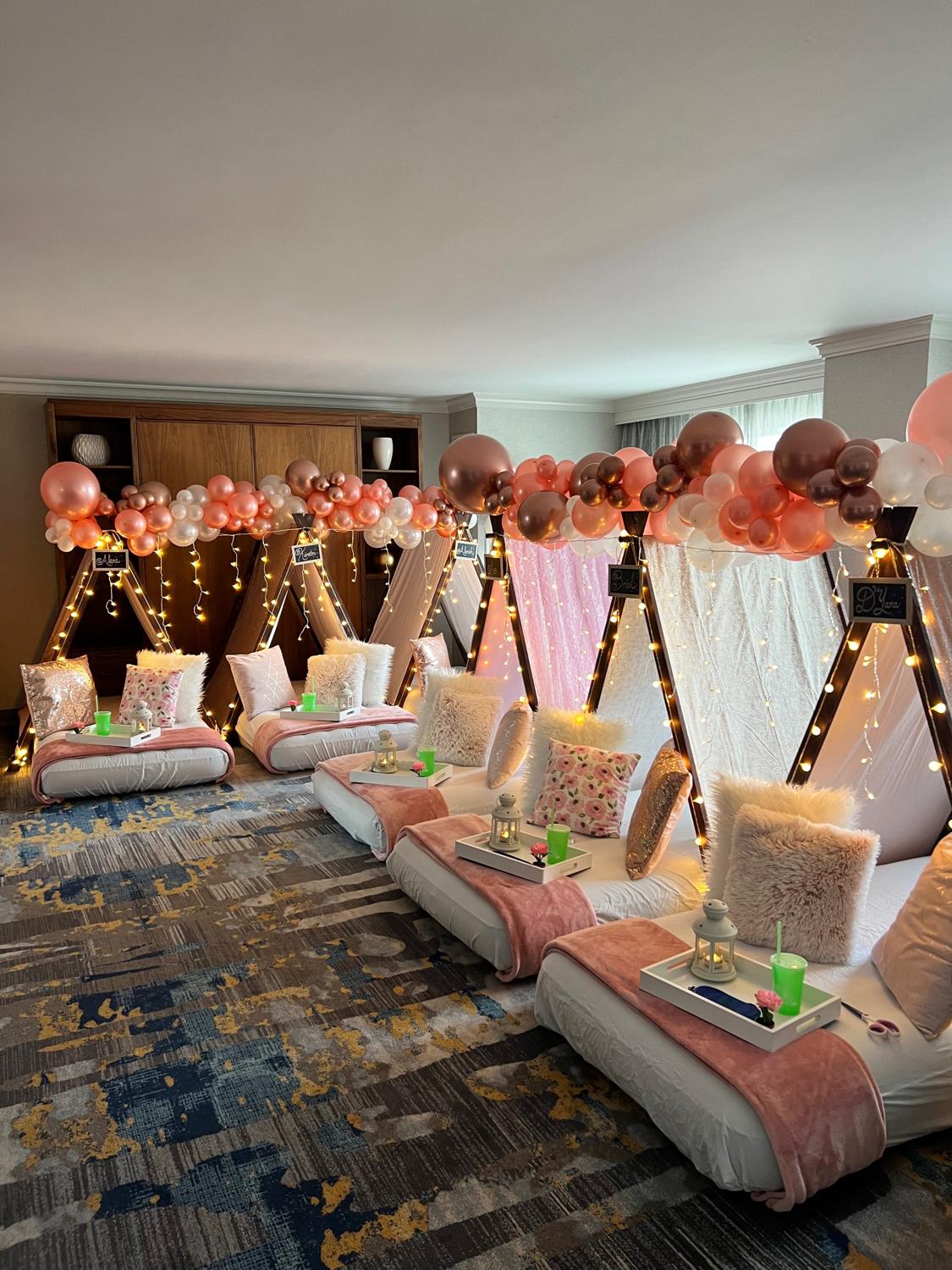 Pink and rose gold sleepover tents styled with blankets, trays, lights and a balloon garland